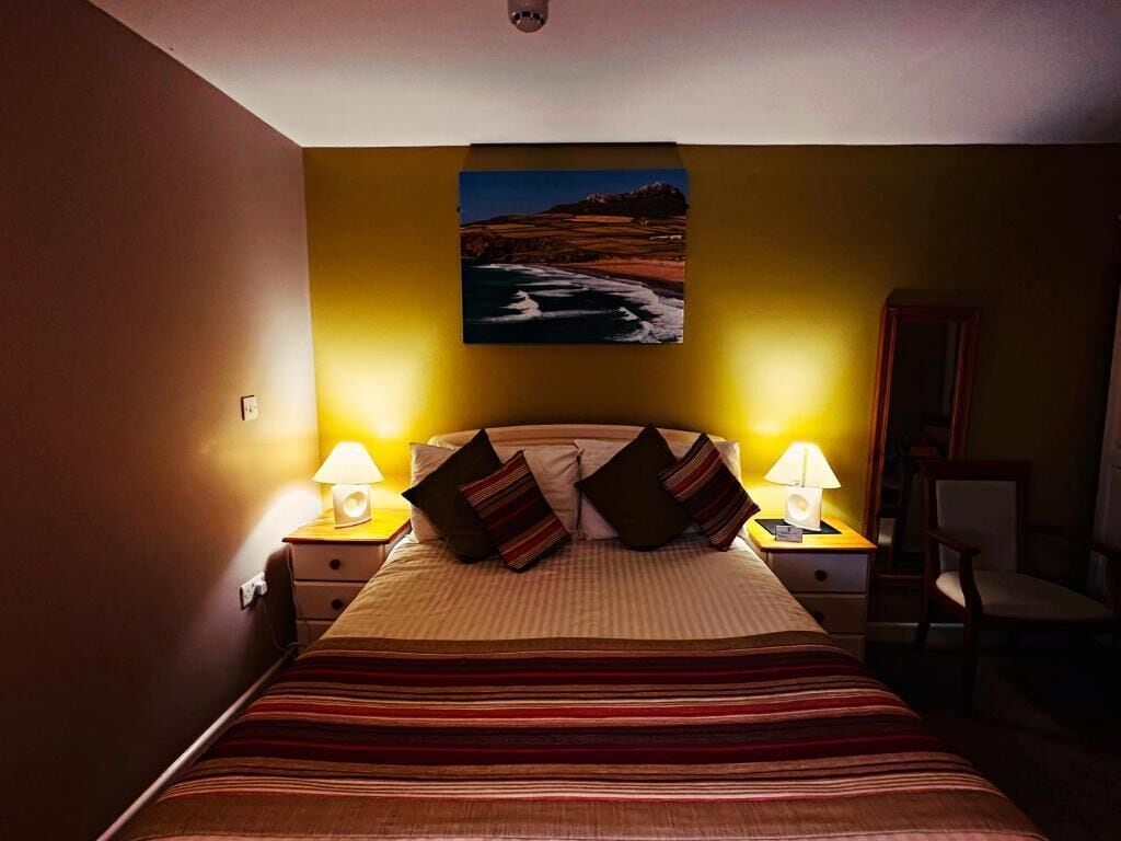 A hotel room with a bed, two bedside lamps, a painting on the wall, and a chair.