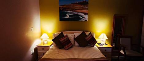 A hotel room with a bed, two bedside lamps, a painting on the wall, and a chair.