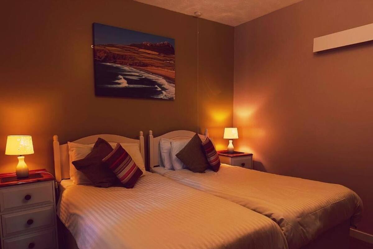 Un lit double avec deux tables de chevet, chacune équipée d’une lampe, dans une chambre où est accrochée une peinture au mur.