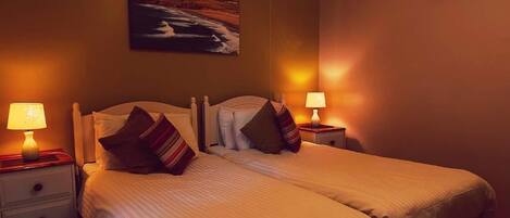 A double bed with two bedside tables, each with a lamp, in a room with a painting on the wall.