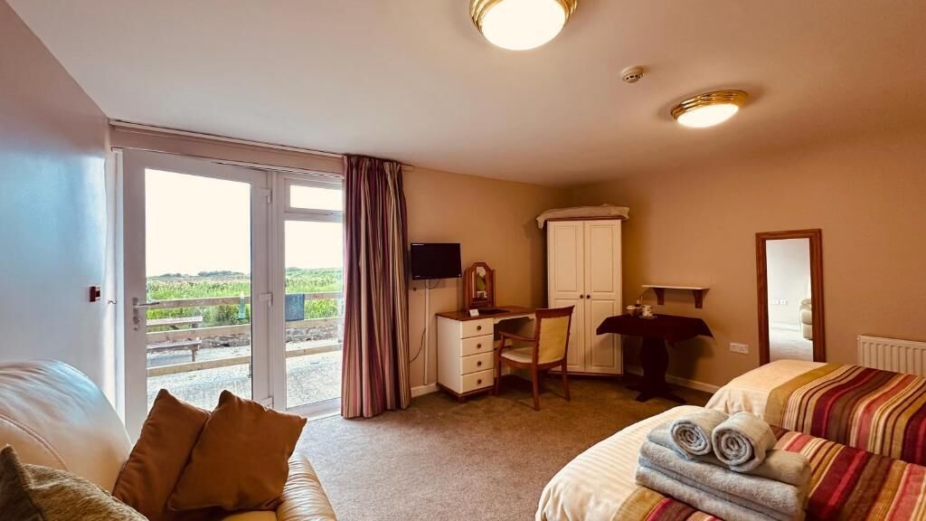 Un dormitorio con cama, escritorio, silla, armario, televisor y una ventana grande con cortinas.