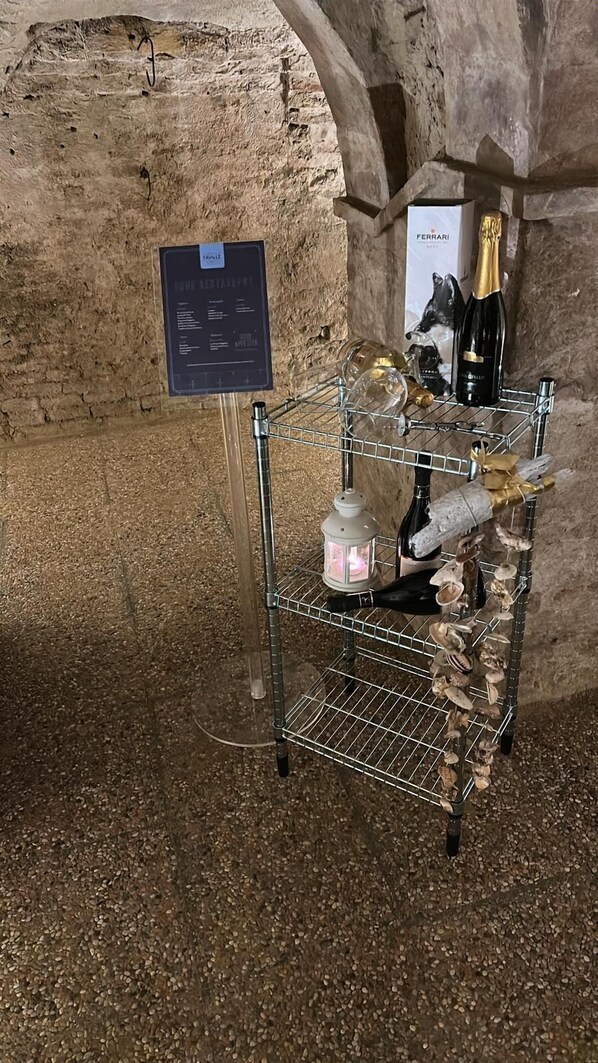 A metal rack with a wine bottle, a lantern, and decorative items in a cave-like setting. - B&B COME NELLE FAVOLE (Saludecio)