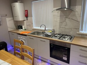 Een moderne keuken met een gasfornuis, een inbouwoven en een raam met zonwering.