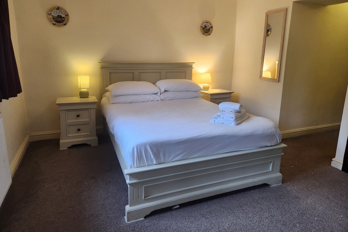 A neatly made bed with white linens and pillows, two bedside lamps, and a small nightstand with a lamp.