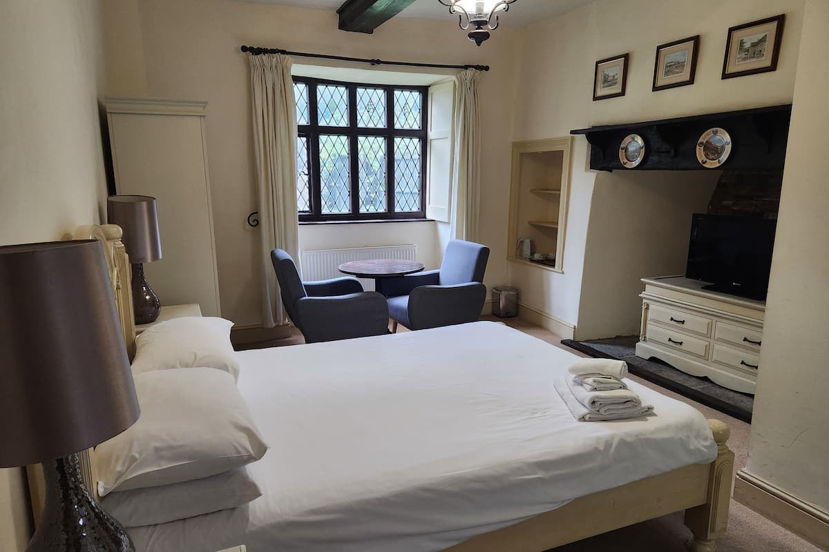 A hotel room with a large bed, a desk with two chairs, a television on a dresser, and a window with curtains.