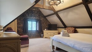 A cozy attic bedroom with a stone wall, a large window, a bed with rolled towels, a TV, and a desk. - Langley Inn (Bristol)
