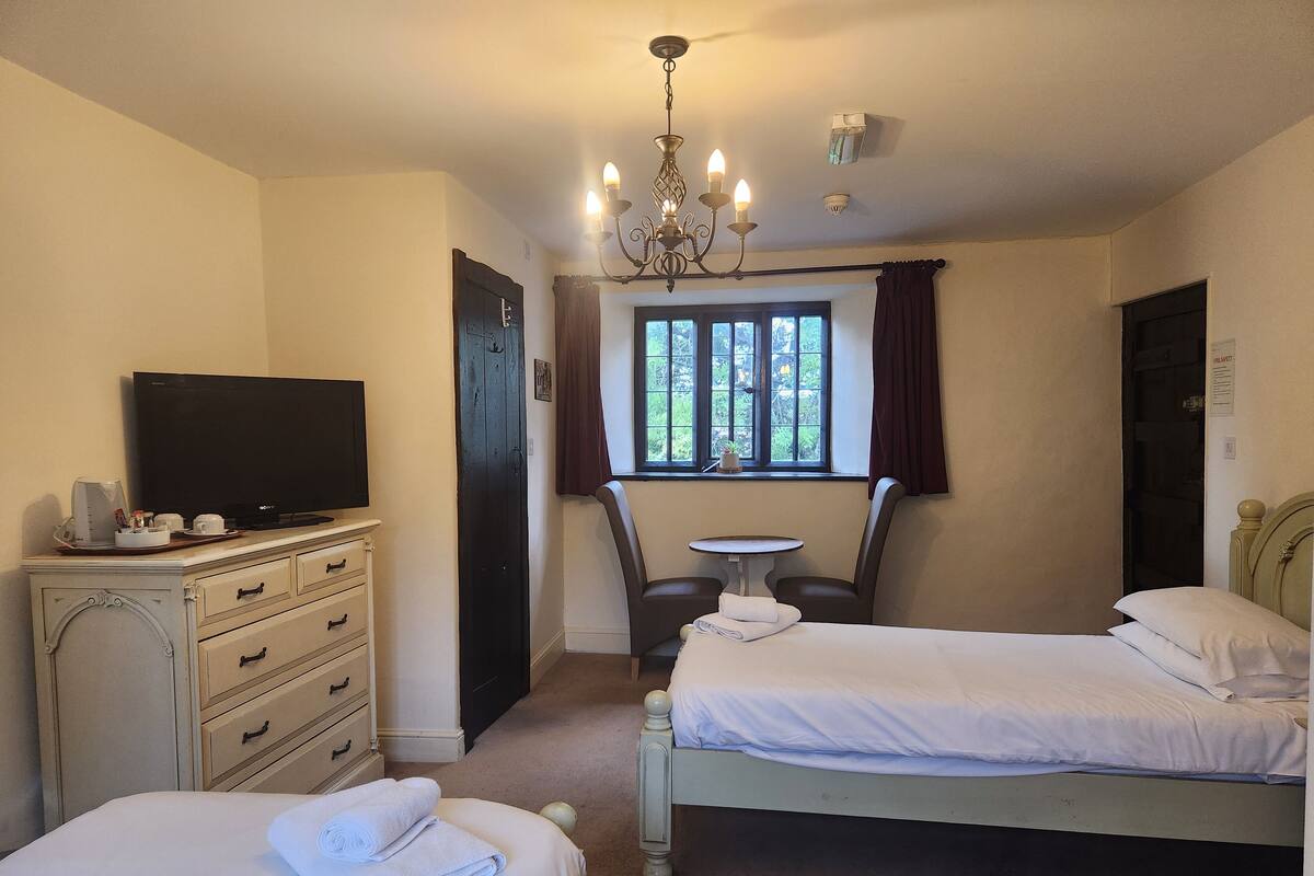 A hotel room with two beds, a television, a dresser, a small table, and a window with curtains.
