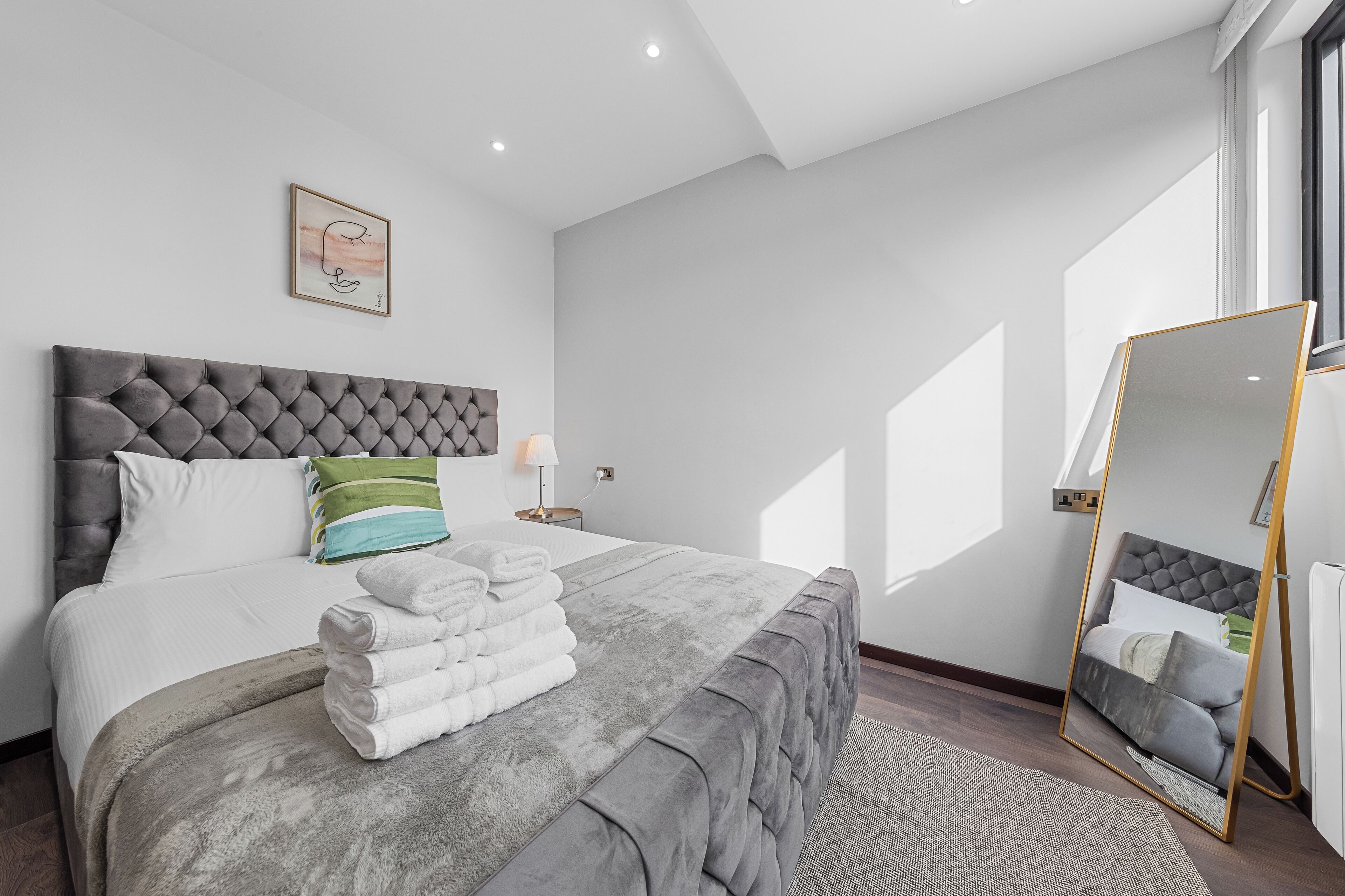 Une chambre moderne avec une tête de lit capitonnée, une pile de serviettes blanches soigneusement pliées et un grand miroir avec un cadre doré.