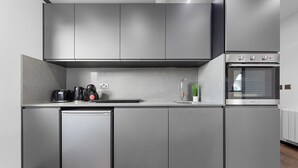 A modern kitchen with grey cabinetry, a built-in dishwasher, a coffee maker, and a stainless steel oven. - Spacious 1-bed Flat in Golders Green Near Station (London)