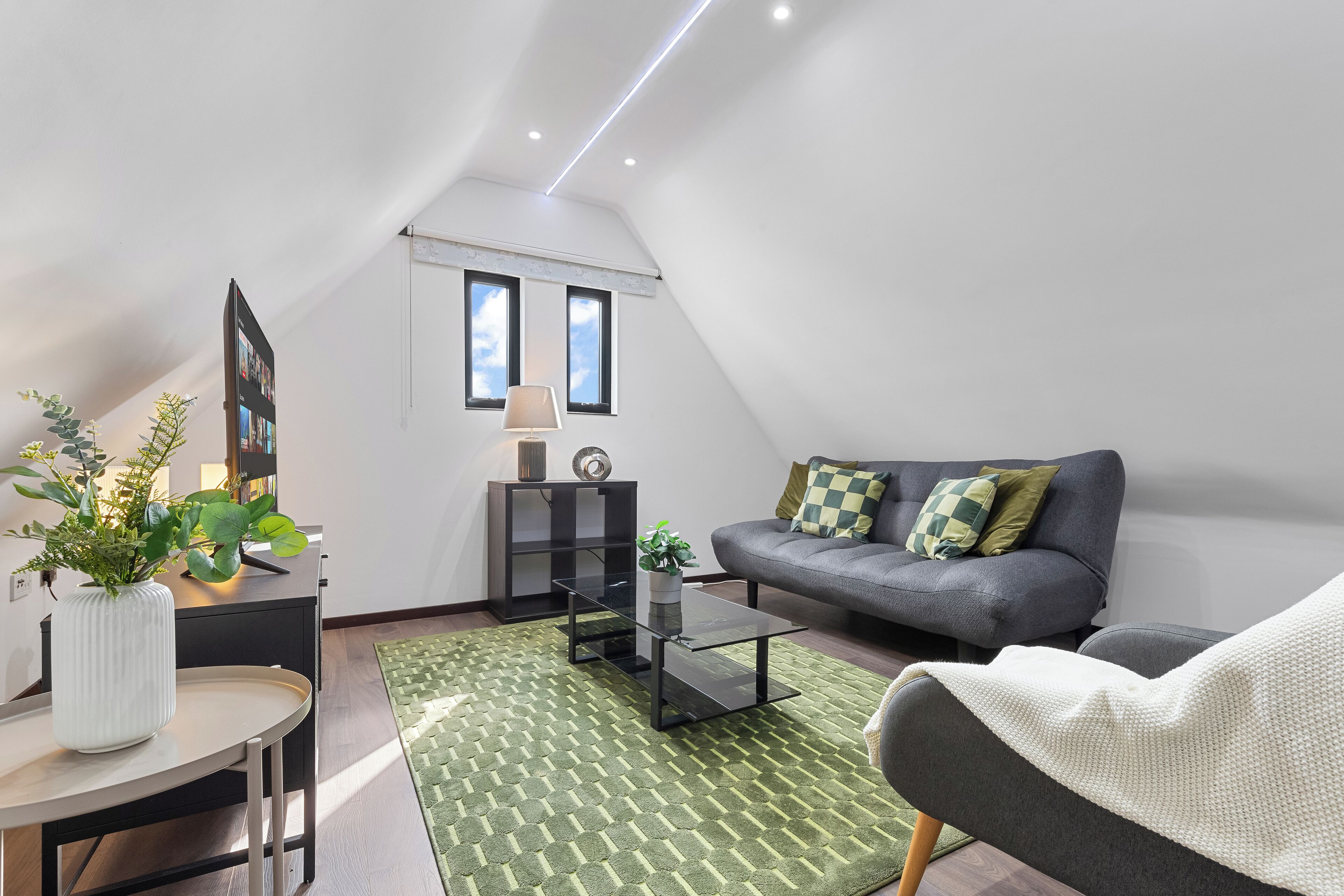 Una sala de estar moderna con un sofá gris, una mesa de centro redonda, un tapete verde estampado y un sillón blanco.