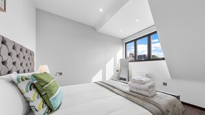 A modern bedroom with a large bed, a window with a view, and a built-in headboard. - Spacious 1-bed Flat in Golders Green Near Station (London)
