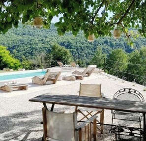 A poolside area with lounge chairs and a table, overlooking a forested hillside. - Villa Mare Motovun - a piece of paradise in the middle of nature  (Motovun)