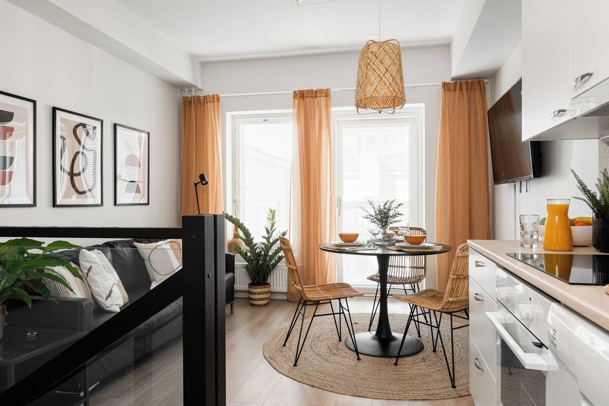 A modern kitchen with a dining area, featuring a round table, chairs, and a hanging light fixture.