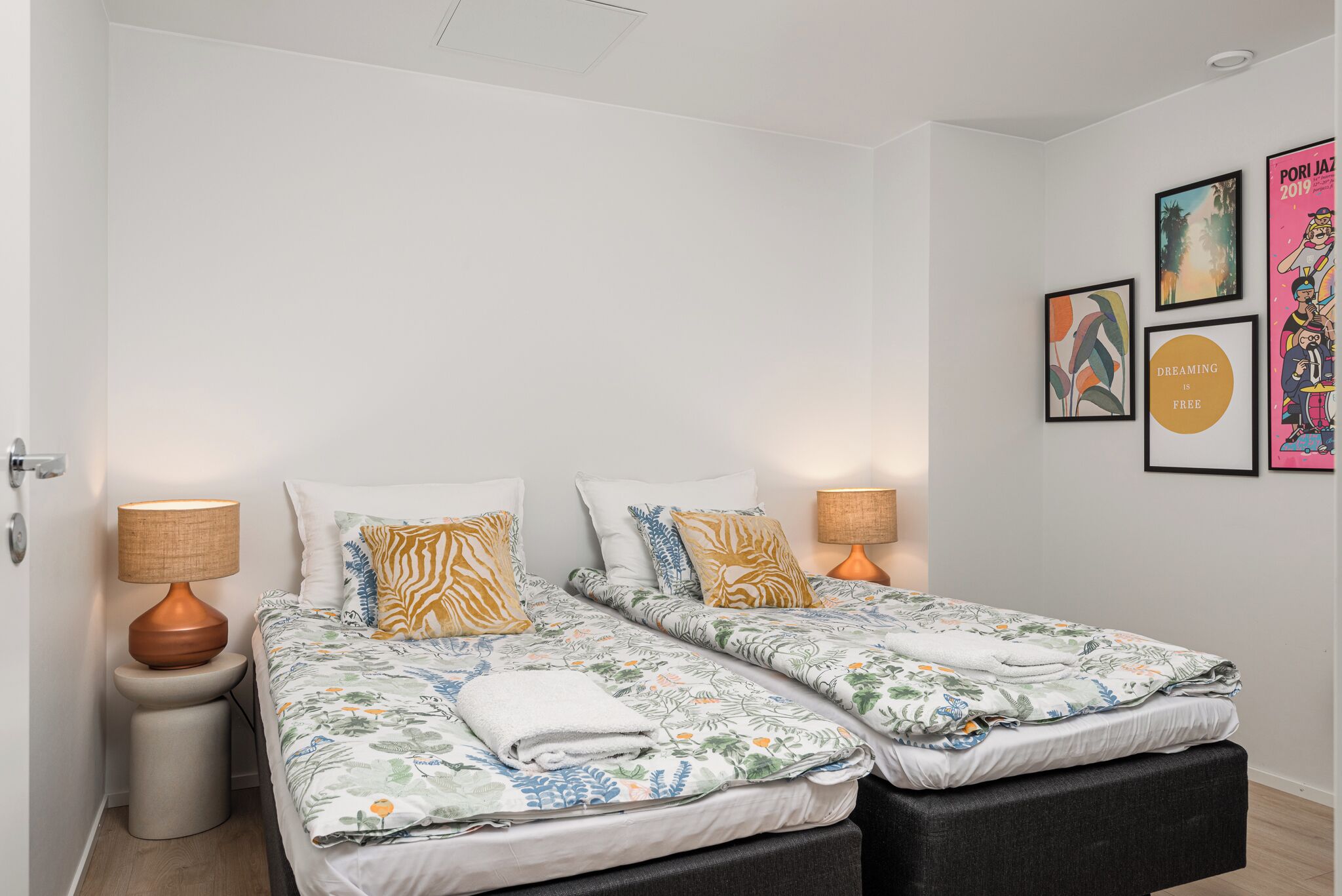 A double bed with floral bedding, two bedside tables with lamps, and a wall with framed artwork.