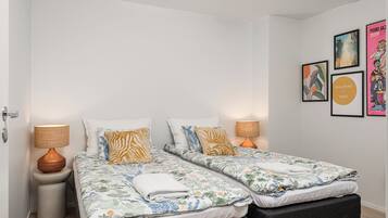 A double bed with floral bedding, two bedside tables with lamps, and a wall with framed artwork.