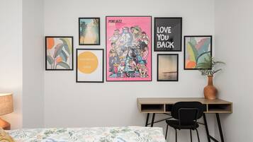 Un dormitorio con cama, escritorio y silla. Seis cuadros enmarcados decoran la pared.