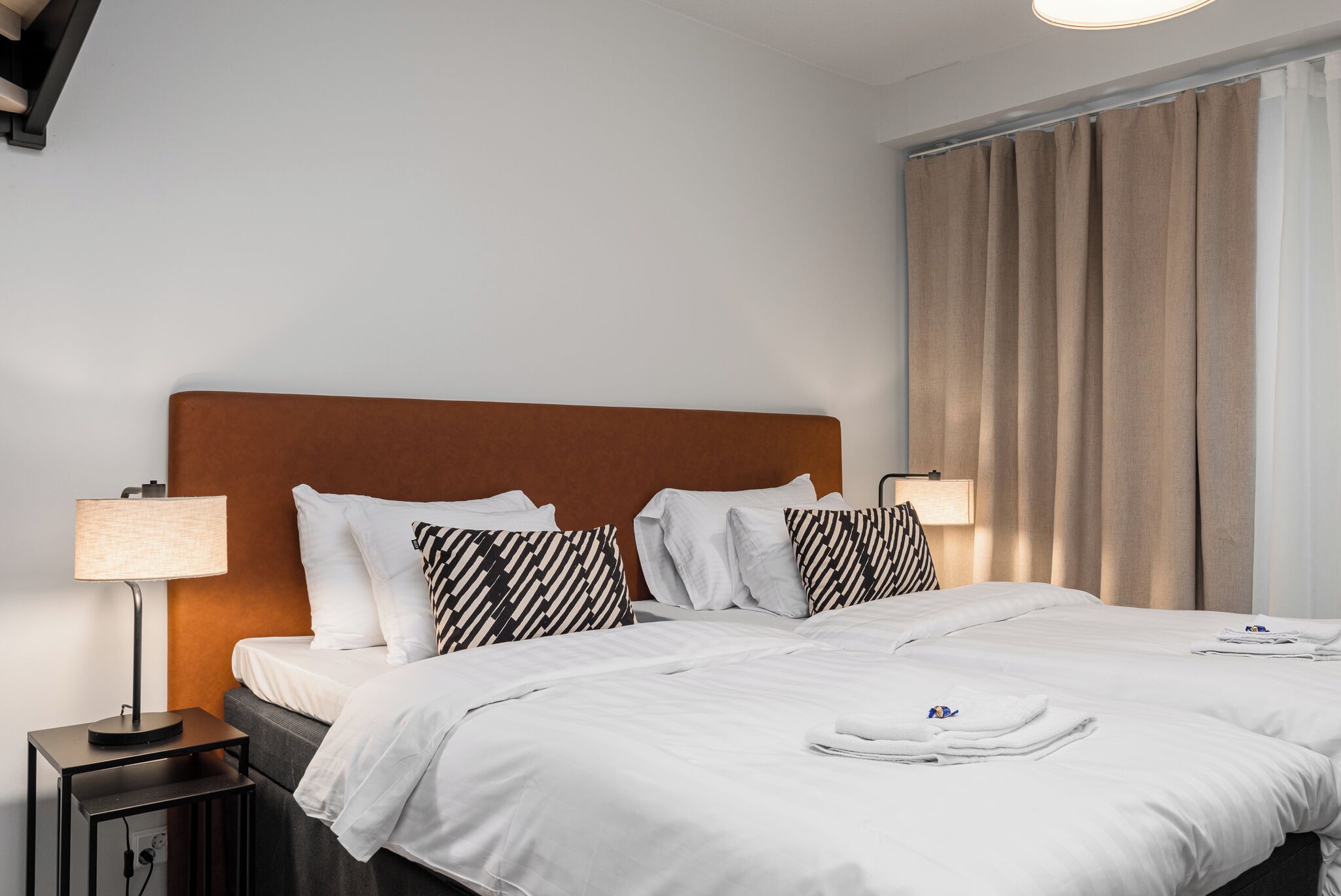 A hotel room with a large bed, two bedside tables, a lamp, and a window with curtains.