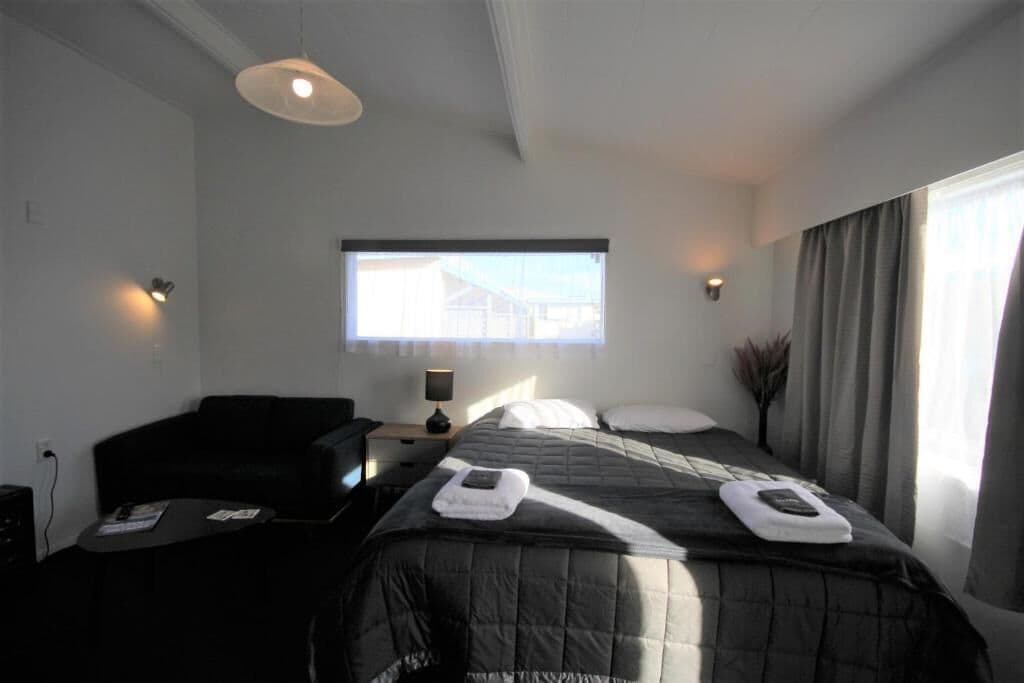 A hotel room with a bed, a desk, a chair, a window, and a nightstand.