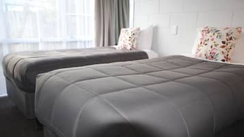 A hotel room with two beds, grey bedding, floral pillows, and a window with curtains.