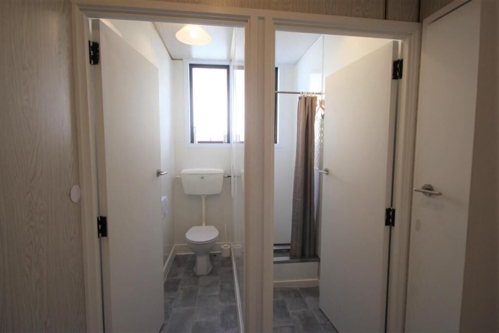 Et badeværelse med toilet, bruser og et vindue med naturligt lys.