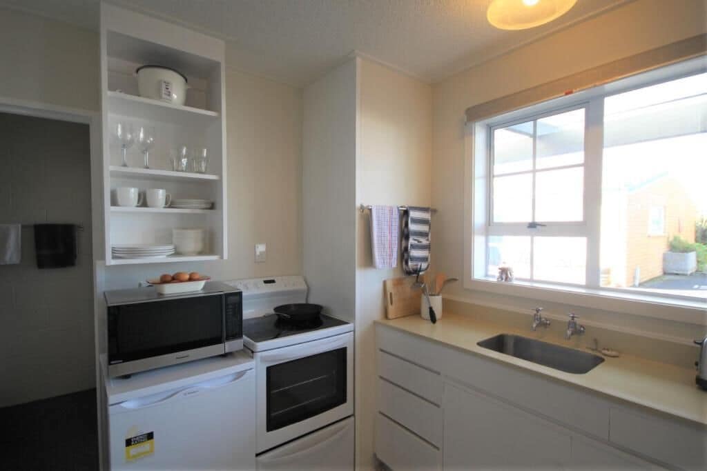 Una cocina con armarios blancos, microondas, horno, fregadero y ventana con vistas al exterior.