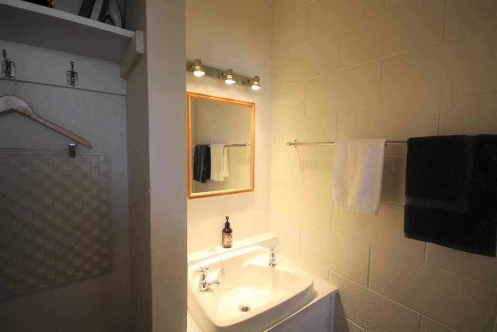 A bathroom with a white sink, a mirror with lights, and two towels hanging on a rack.