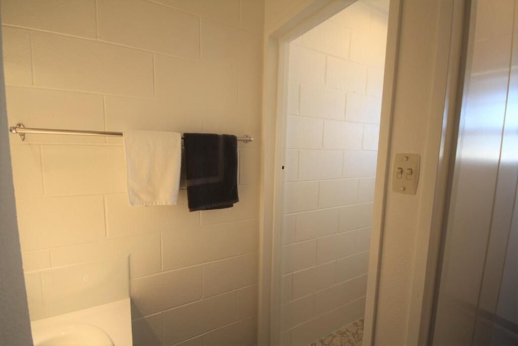 A bathroom with white tiled walls, a white toilet, and a towel rack with two towels.