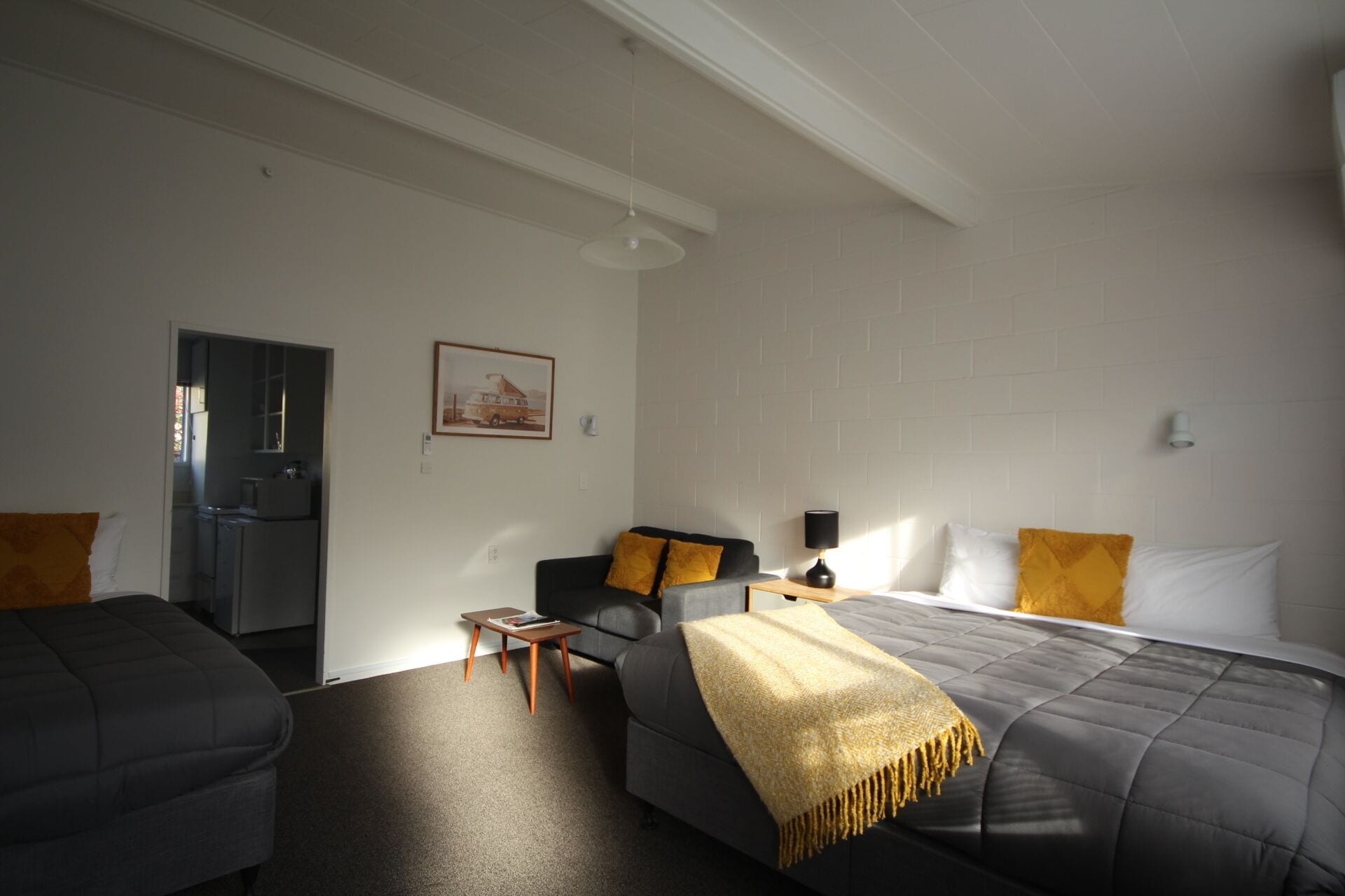 Una habitación de hotel moderna con una cama grande, un sofá, una mesita y una kitchenette al fondo.