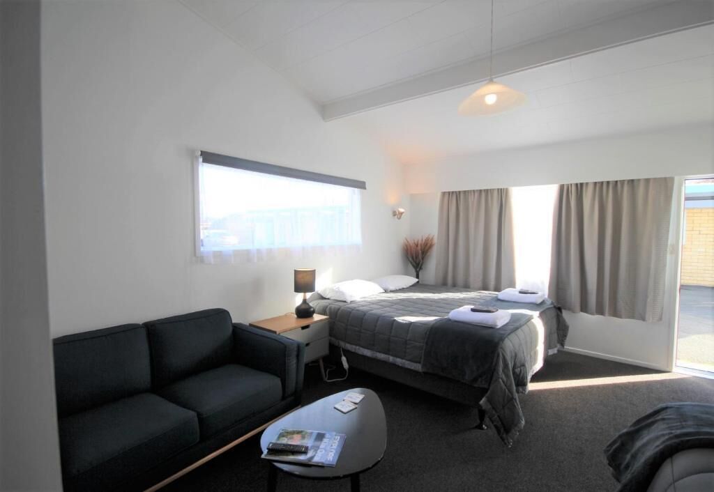 Una habitación de hotel moderna con una cama, un sofá, un escritorio y una ventana con cortinas.