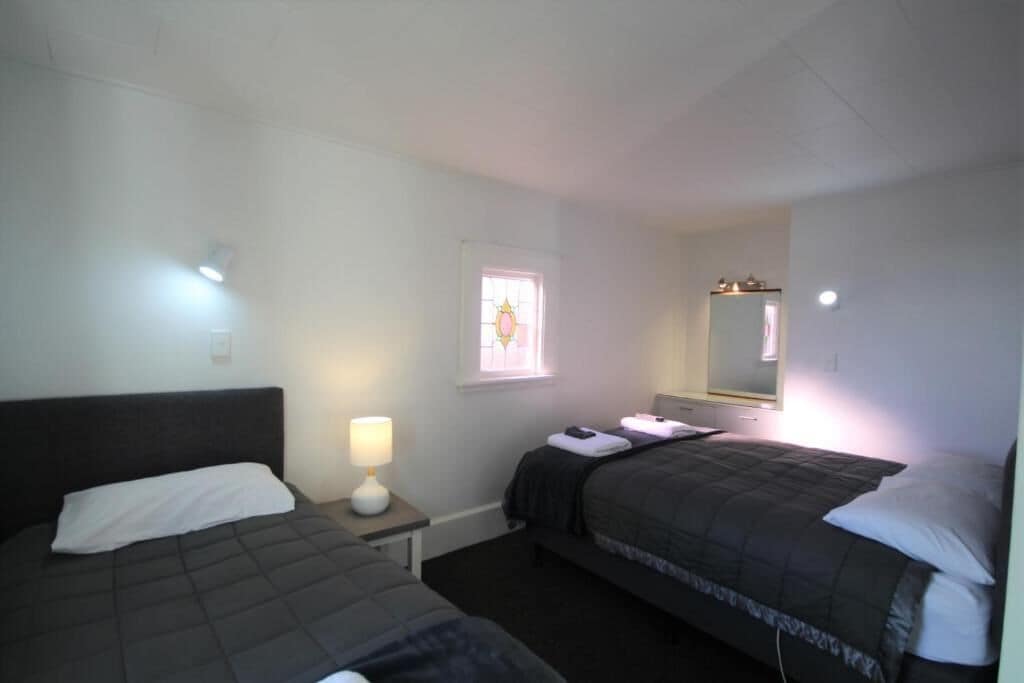 A bedroom with two beds, a bedside table with a lamp, a window with a view, and a mirror on the wall.