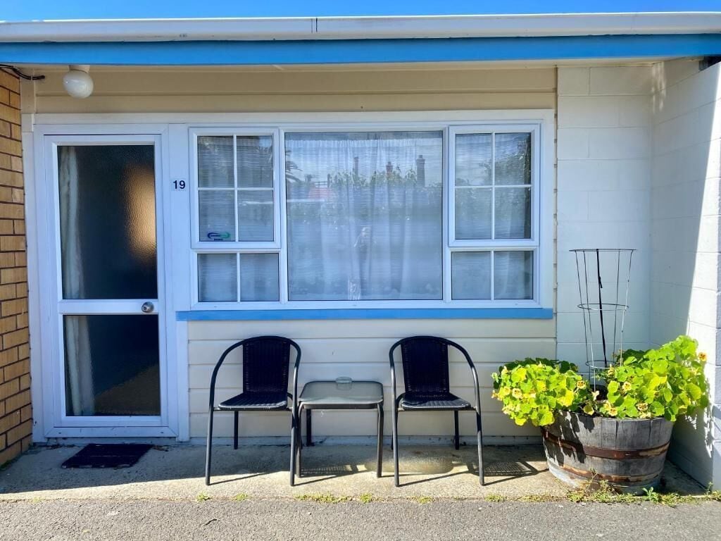 A building with a blue and white exterior, a large window with a number 19, two chairs, a small table, and a potted plant.