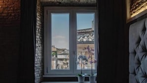 A room with a stone wall, a window with a view of buildings, a bed with a headboard, and a radiator below the window. - Rhome Luxury suite (Rome)
