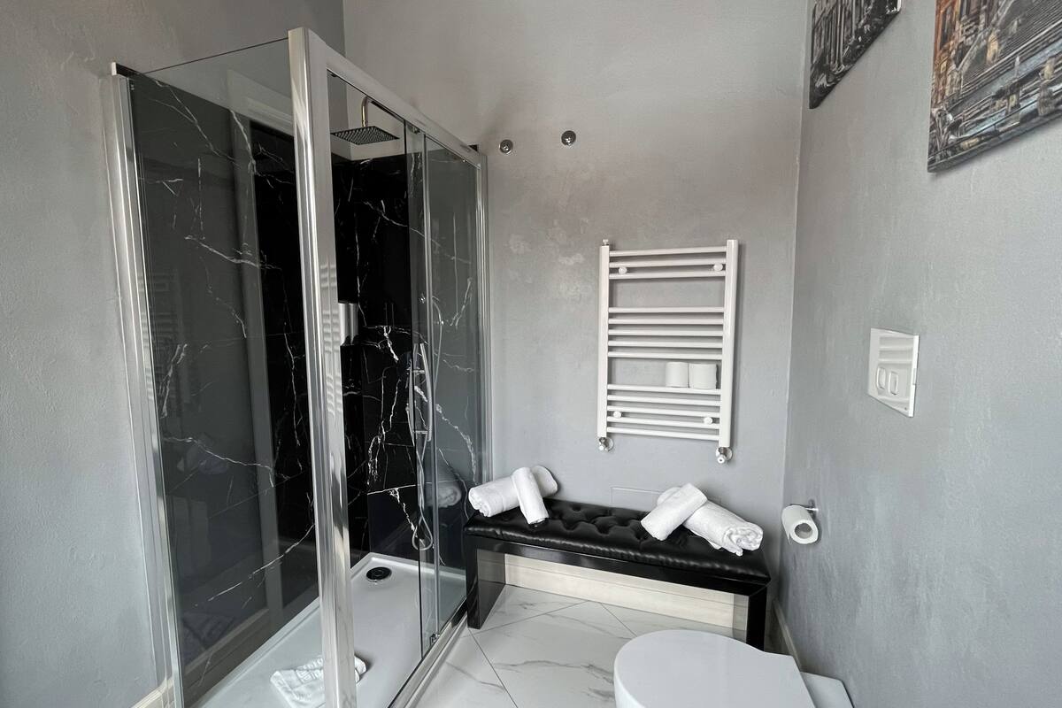 A modern bathroom with a glass-enclosed shower, a white toilet, and a bench with towels.
