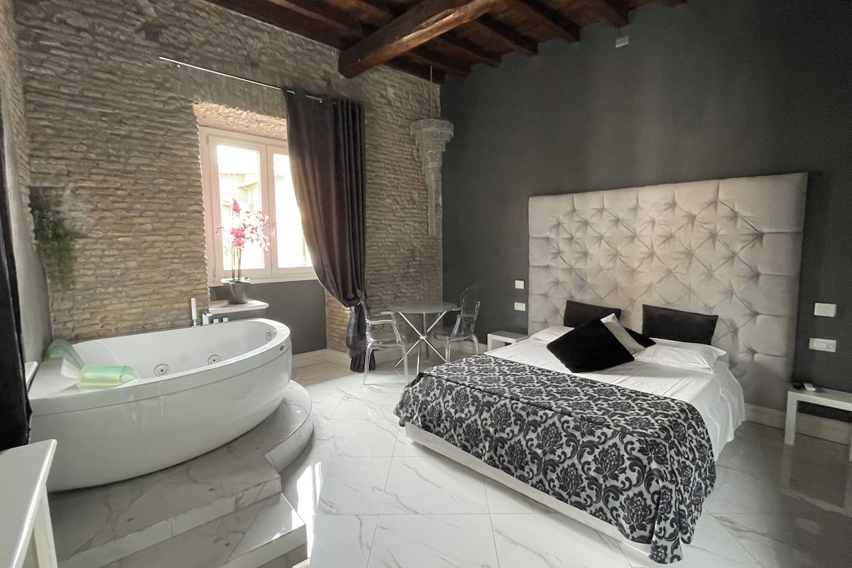 A modern bedroom with a large bathtub, a tufted headboard, and a marble floor.