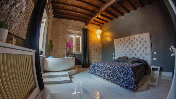A bedroom with a large bed, a bathtub, and a stone wall. - Rhome Luxury suite (Rome)