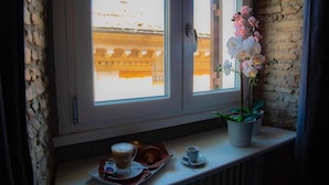 A window with a view of a building, a potted orchid, and a tray with a cup and pastry. - Rhome Luxury suite (Rome)