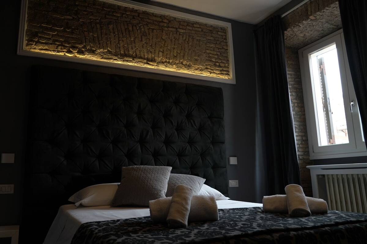 A bedroom with a dark headboard, a bed with white linens, and a window with curtains.
