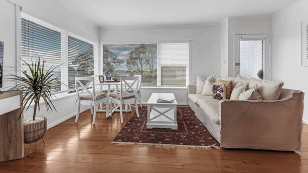 A living room with a white sofa, a coffee table, and a dining area with a white table and chairs.
