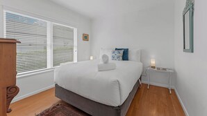 A bedroom with a large bed, a bedside table with a lamp, a small bedside table with a lamp, and a picture on the wall.