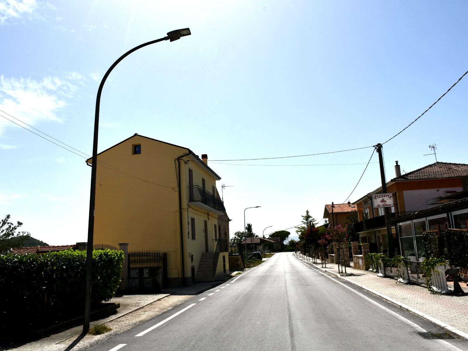 A street with a yellow building, a street lamp, and a sign for a pizzeria.