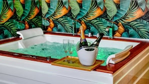 Un bain à remous avec du champagne et des verres, le tout installé devant un mur couvert de verdure.