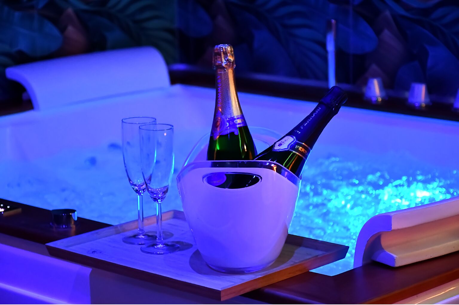 A room with a jacuzzi tub, two champagne flutes, and two bottles of champagne in a bucket.