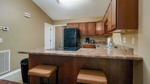Una cocina con armarios de madera, un refrigerador negro, una estufa y una encimera con dos taburetes.