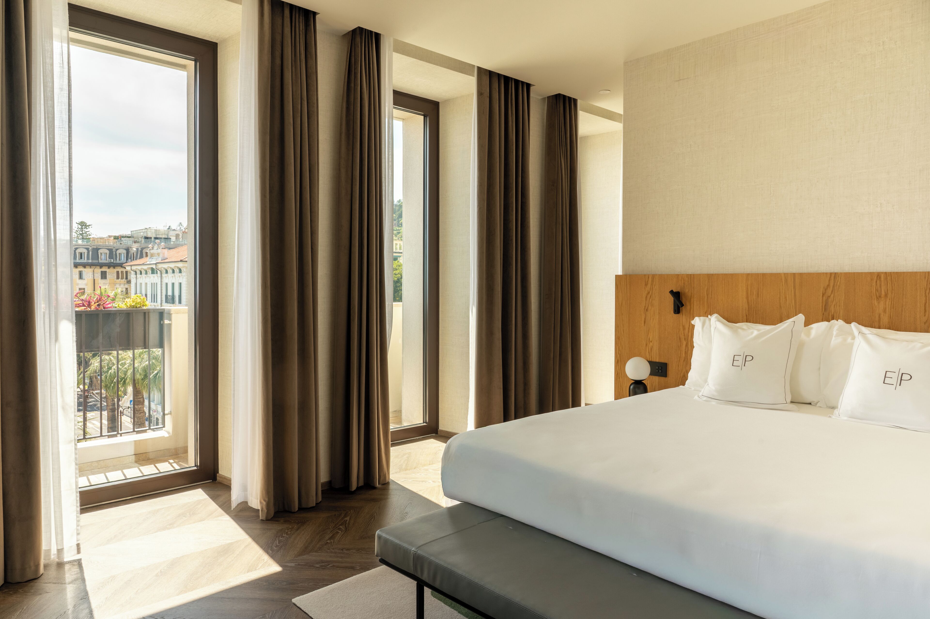 Une chambre d’hôtel avec un grand lit, une tête de lit en bois et une vue sur les immeubles par la fenêtre.