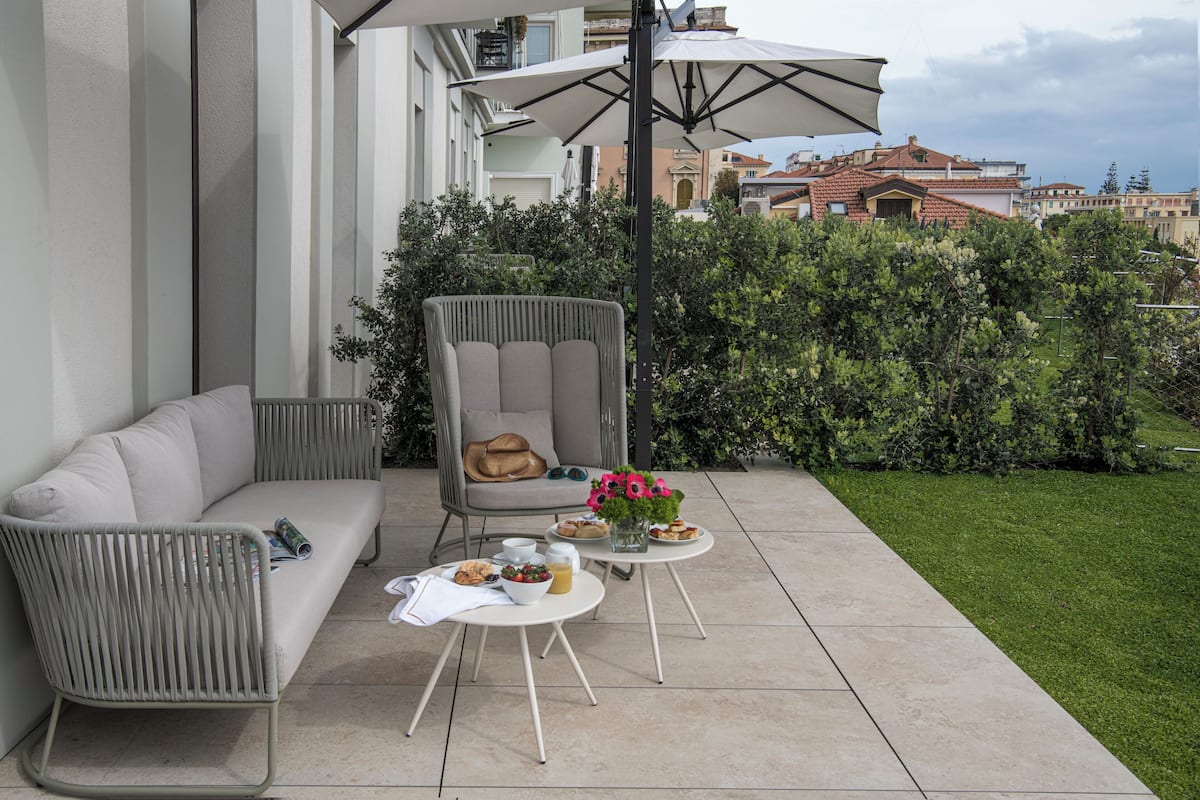 A patio with a white sofa, a grey armchair, and a small round table with food and drinks.