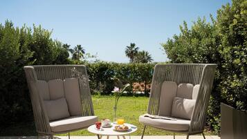 Two wicker chairs with cushions, a small round table with a drink, a pastry, and a glass of orange juice.