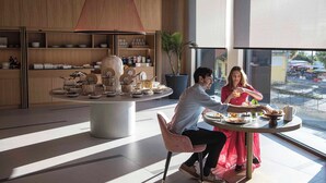 Un espace repas moderne avec une table ronde, un grand luminaire suspendu et une vue sur la rue.
