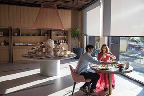 Un espace repas moderne avec une table ronde, un grand luminaire suspendu et une vue sur la rue.
