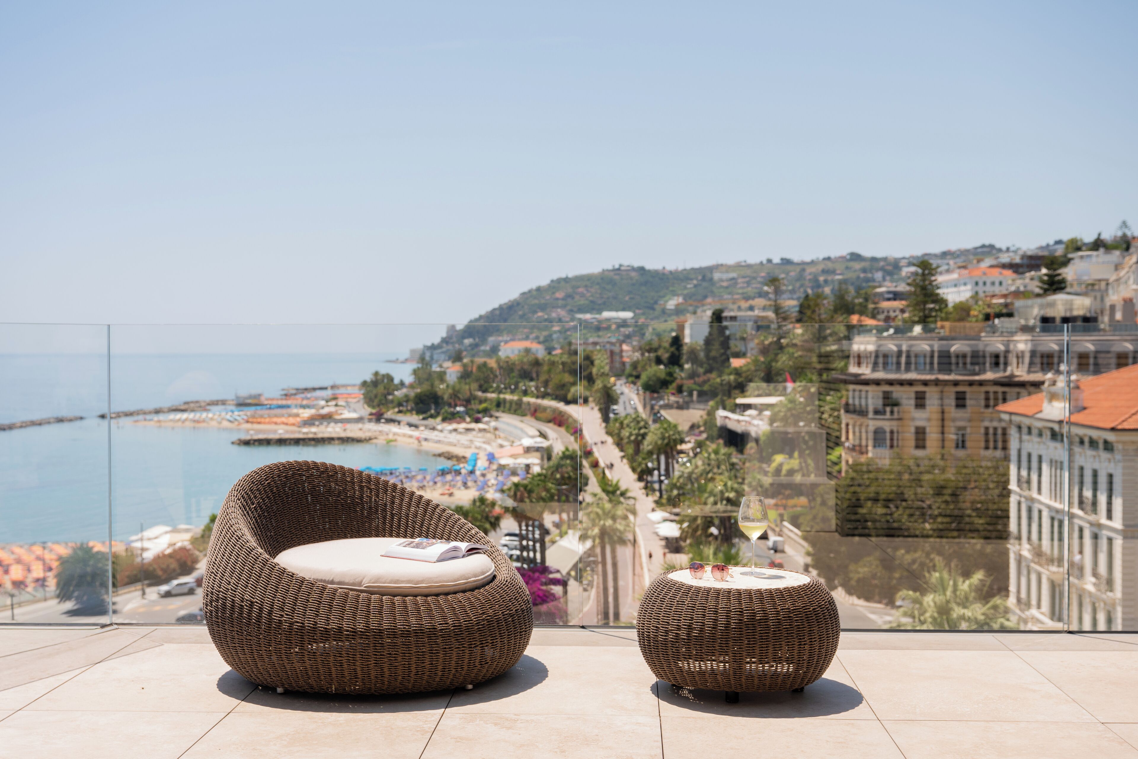 A balcony with wicker furniture overlooking a coastal cityscape.