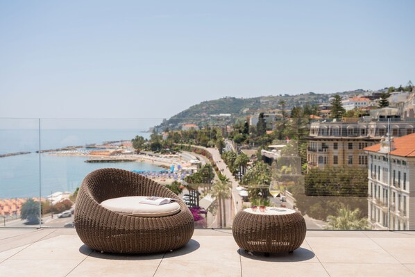 A balcony with wicker furniture overlooking a coastal cityscape.